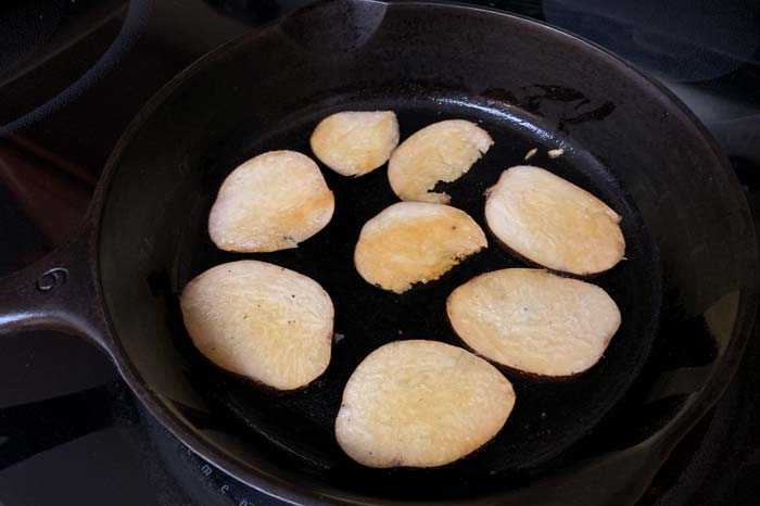 Slices of pre-boiled American groundnuts sizzling in a cast iron pan.