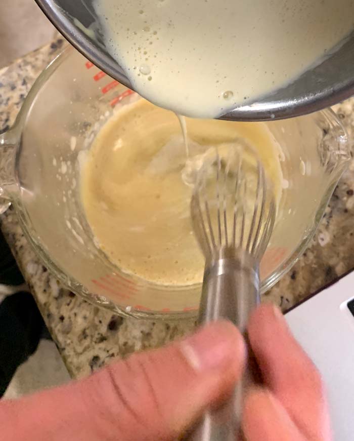 Slowly pouring the hot cream into the egg mixture while whisking vigorously prevents the eggs from scrambling and clumping.