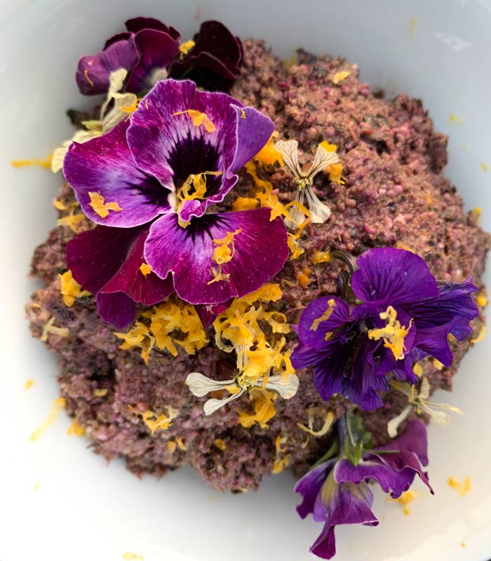 Purple kale pesto garnished with Meyer lemon zest and seasonal flowers (pansies, arugula, rosemary).