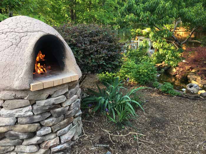 Our back yard in summer during a cob oven cook. You can see our ducks swimming in their pond in the background underneath a large peach tree. Behind that, you can make out part of the 6' tall wood fence.
