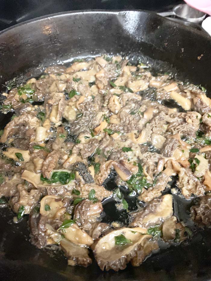 Morels finishing cooking in a cast iron pan on our stovetop. Once the water is almost finished cooking out, you'll start getting some pops as the remaining liquid is sent fleeing by the hot butter. That means you're 1-2 minutes from being done with the morels, but you'll need to cool them to at least room temperature before blending with cheese and other ingredients.