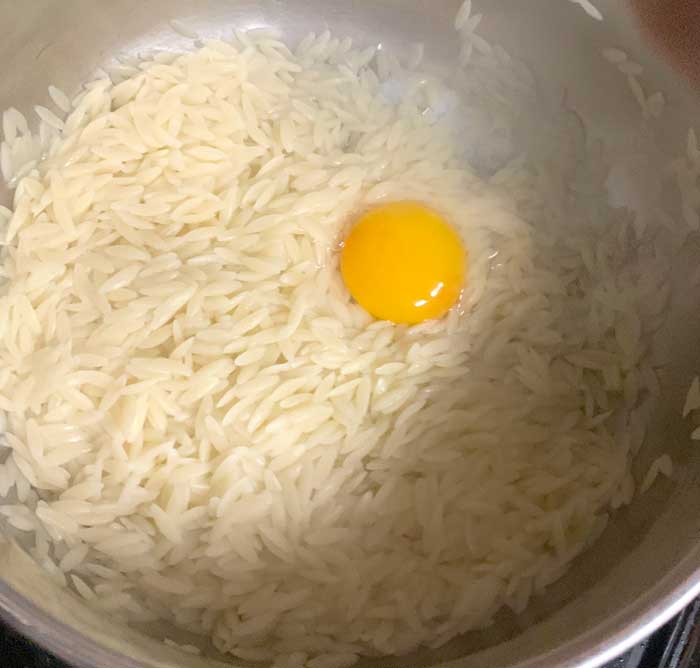 A whole duck egg added to steaming hot orzo - stir, stir, stir!