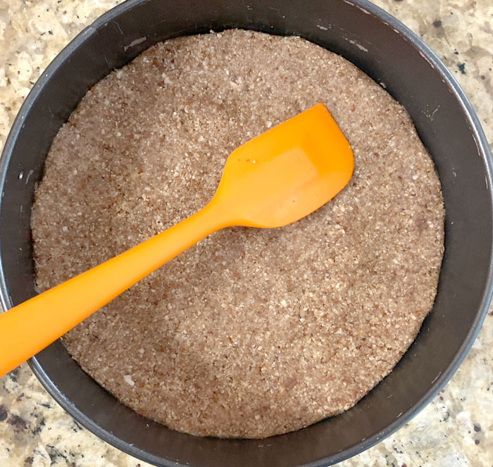 Flatten and even out the nut crumble by hand or with a spatula to form the cheesecake crust. Then into the oven for toasting!