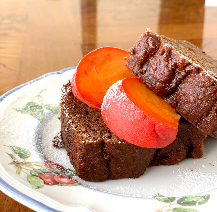 Spiced persimmon bread garnished with slices of ripe persimmons and a dusting of powdered sugar.