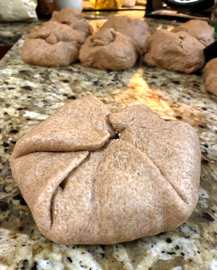 A folded poğaça ready for an egg wash + seed coating.