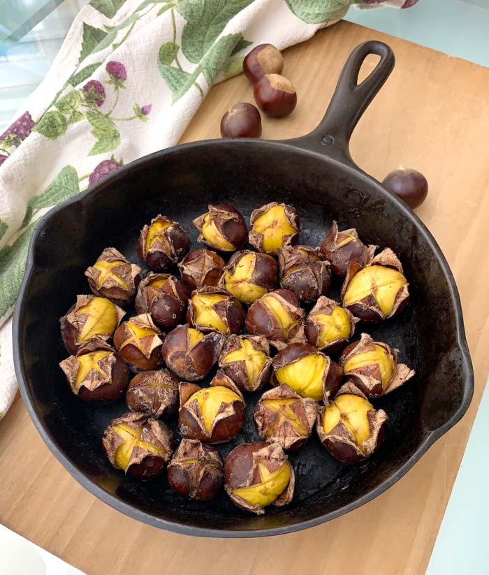 Turn each chestnut cut side up for most visual appeal. We also like to serve them in the same cast iron pan they were cooked in, communal style. Dinner guests can pull each one out as they go. Chestnuts roasted in a cast iron skillet on a stove top.