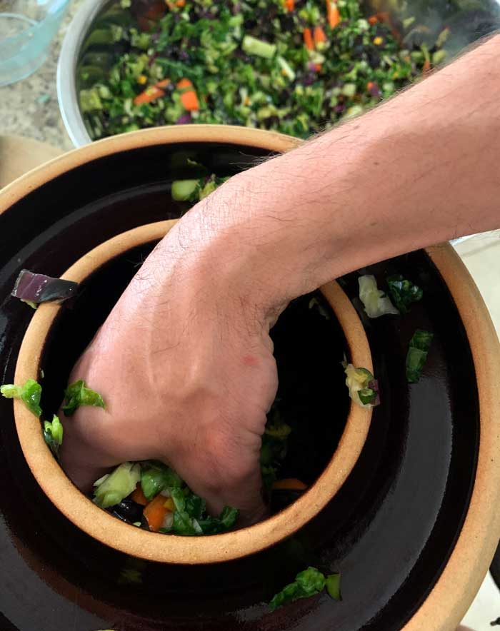 Filling our fermentation crock with garden-fresh ingredients to make another round of sauerkraut.