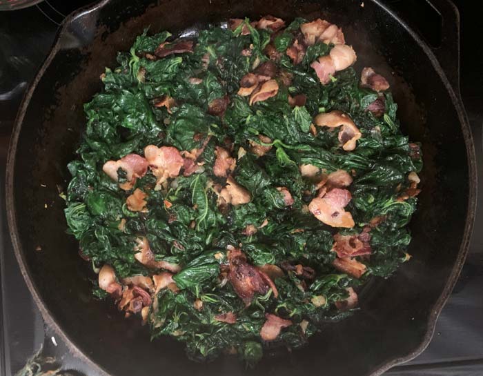 Cooked stinging nettle mixture evenly distributed on bottom of pan in preparation for eggs.
