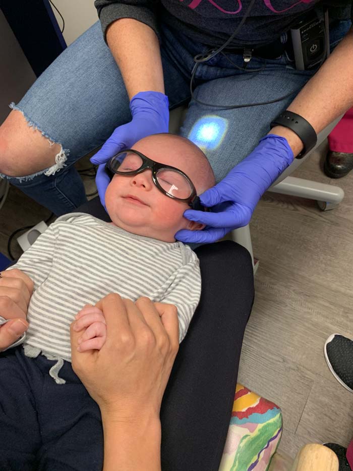 Sebastian laying on Susan's lap for his frenectomy - a procedure to remove his tongue-tie and lip-tie. His eyes are closed because of the bright lights, not because he is sedated. Dr. Bynum's dentist office is decorated like a fun beach resort and the staff doesn't wear clinical gear (she's wearing some stylish torn jeans in this photo). This environment helps older kids feel more comfortable there.