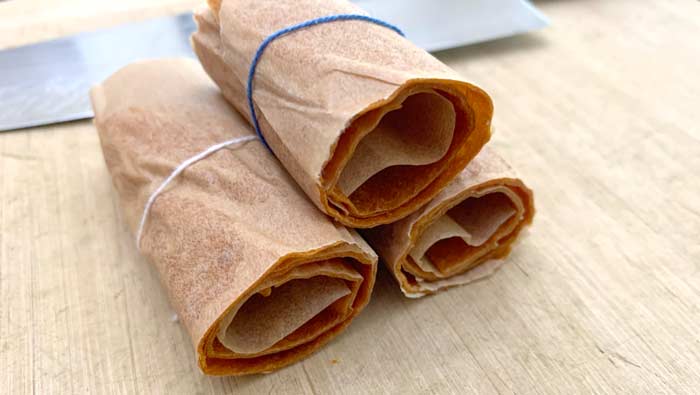 Rolls of finished peach fruit leather rolled, tied, and cut inside the parchment paper they were dried in.